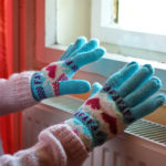 Hands in wool gloves on radiator