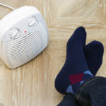 Feet in woolen winter warm socks near electric fan heater at home.