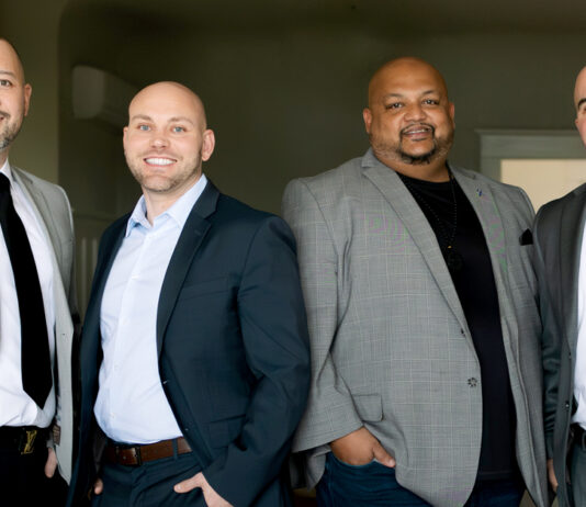 Four professional real estate brokers standing in business attire; from left to right are Jason Liberty, Tim Bower, Ameet Prasad, and Robert Covais